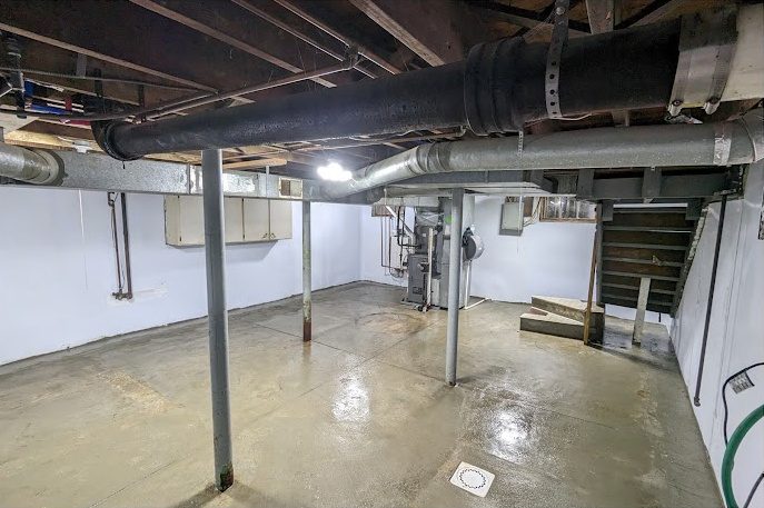 White-lined basement walls with steel posts, ductwork and the stairs beyond
