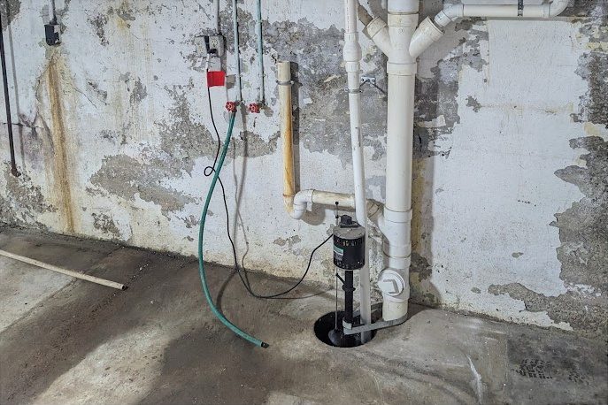 Before: an exposed sump pump in an open pit against a stained block wall