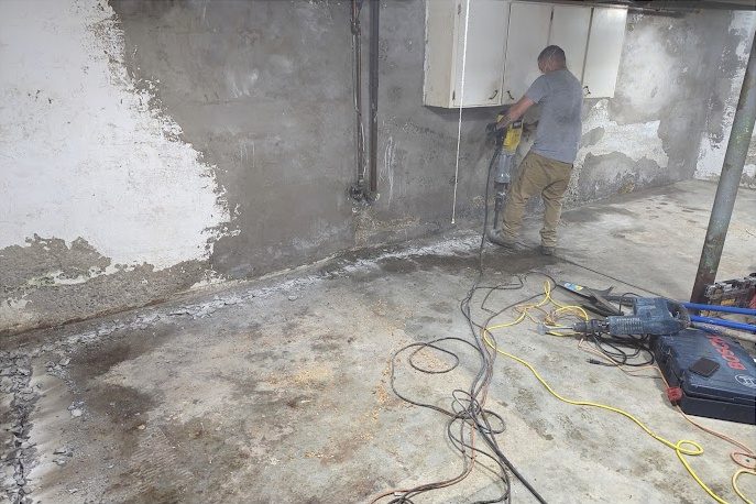 Before: a technician working at a block wall with old white paint and dark staining