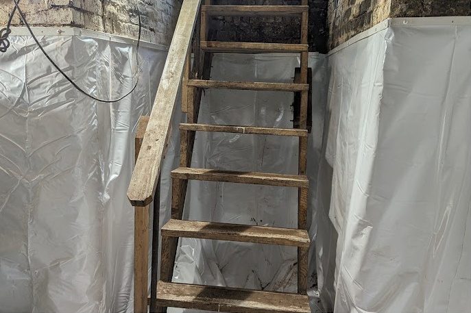 A wooden basement stair with white liner on the walls either side