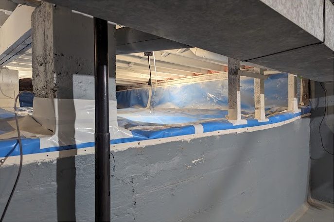 A lined crawl space above a basement wall, with blue tape along the top