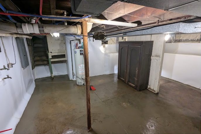 A basement with white-lined walls and a fresh floor around the water heater and a cabinet