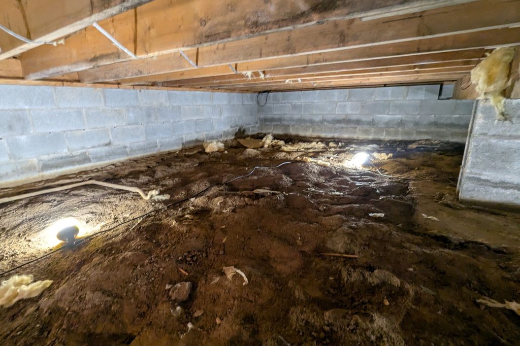 Before: bare ground and rubble under exposed joists, with old insulation between them