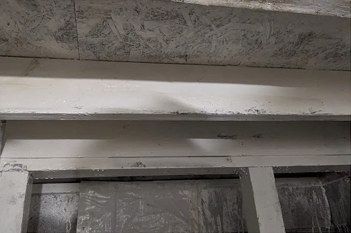 Joists and a beam coated white above a crawl space wall