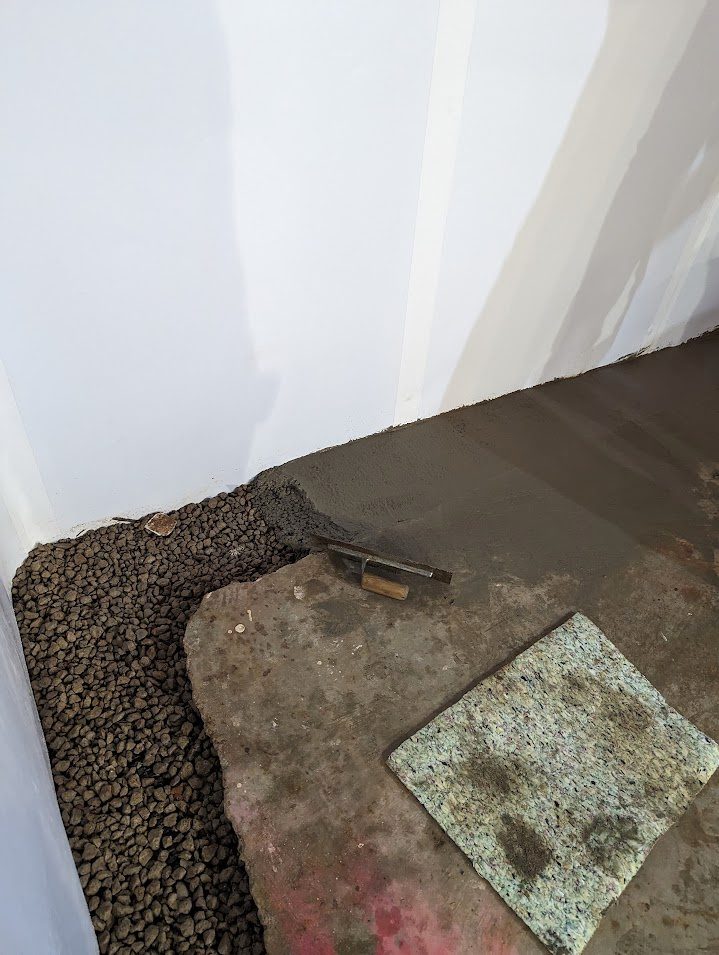 Fresh floor patch beside open gravel channel and wall liner