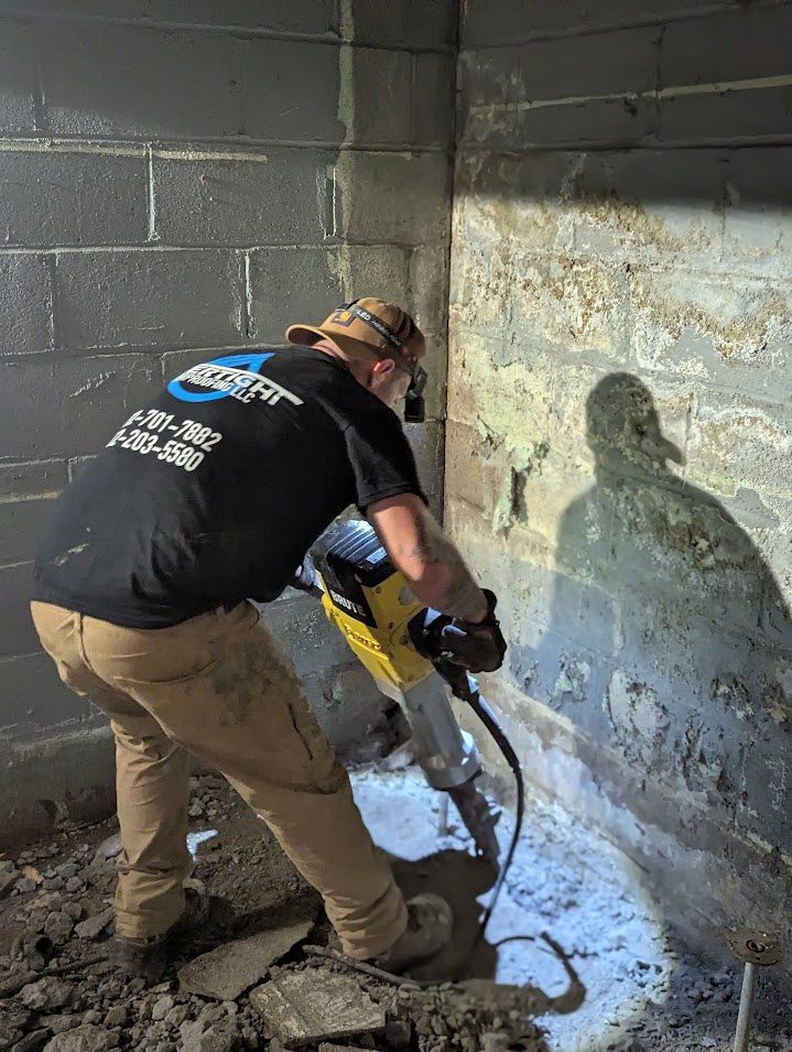 Worker using demolition tool along basement perimeter