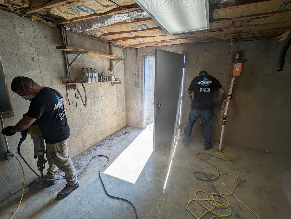 Two workers opening basement perimeter near a doorway