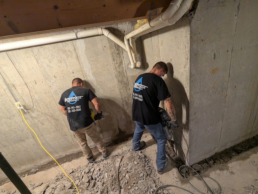 Two Watertight workers using tools along a basement wall