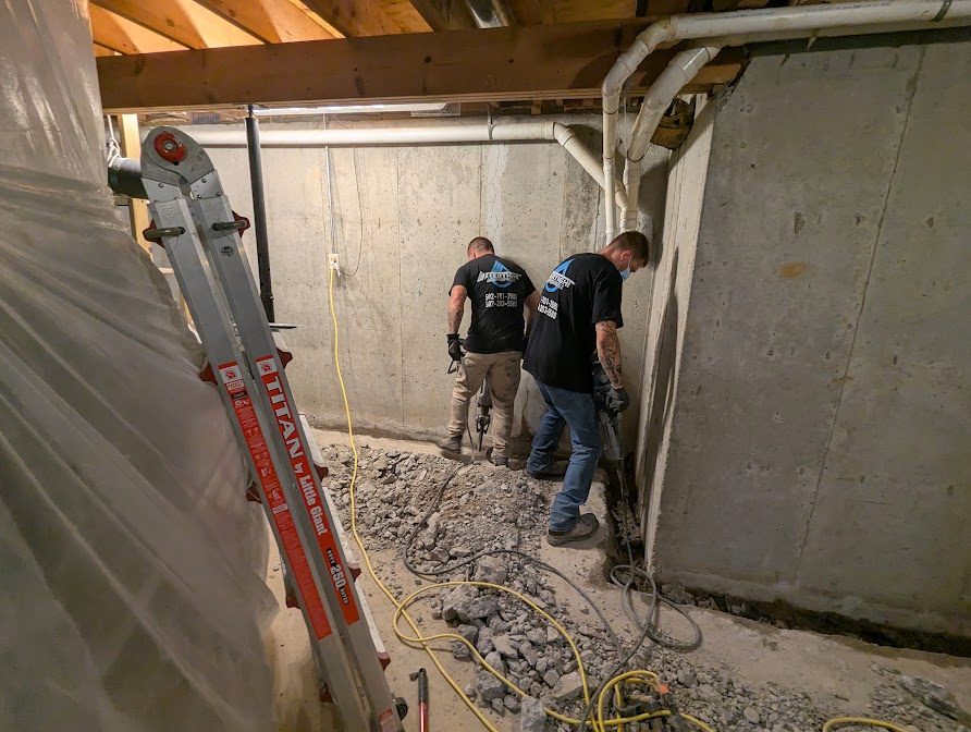 Two workers breaking floor beside basement wall