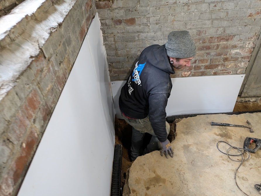 Worker fitting white liner to brick basement wall