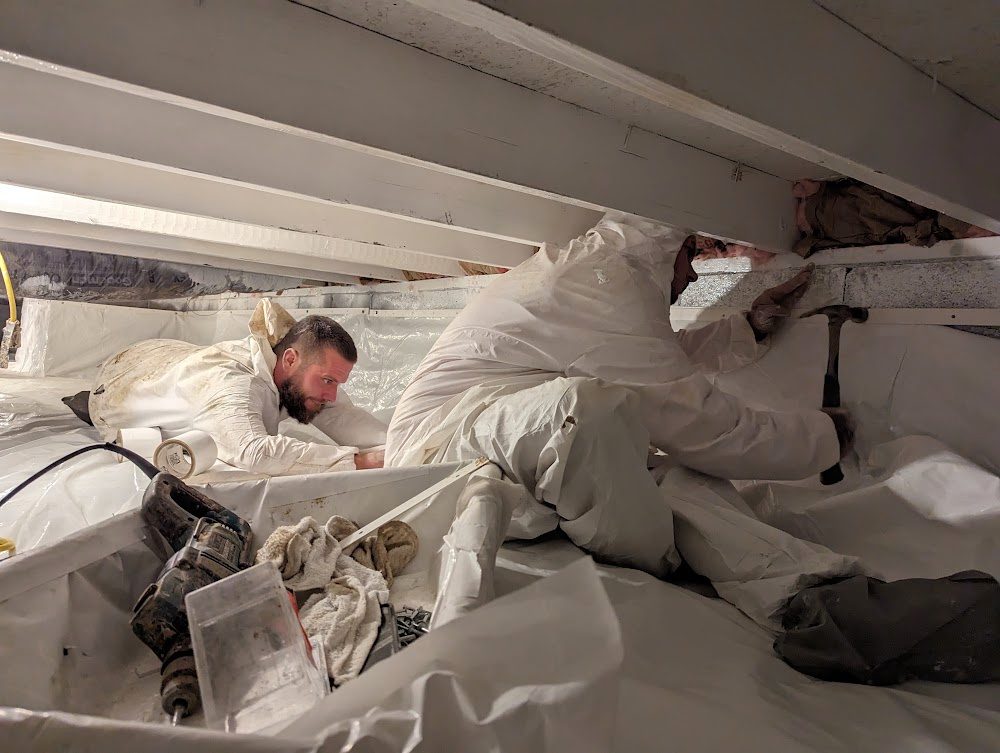Two coveralled workers fitting crawl space lining
