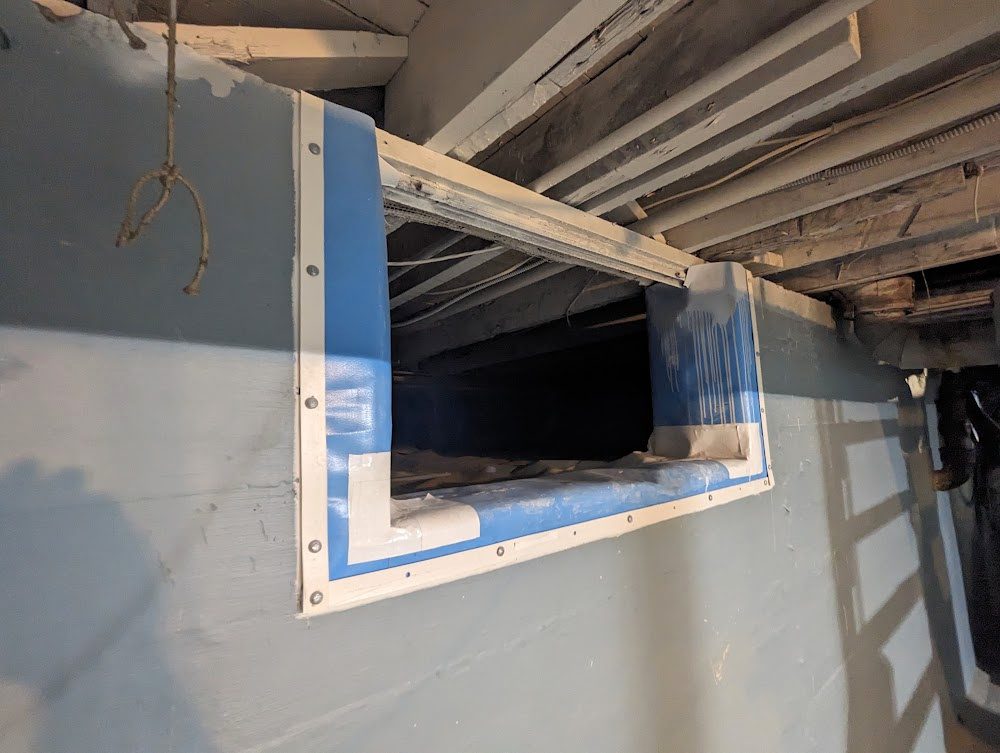 Crawl space access opening framed by liner with blue tape