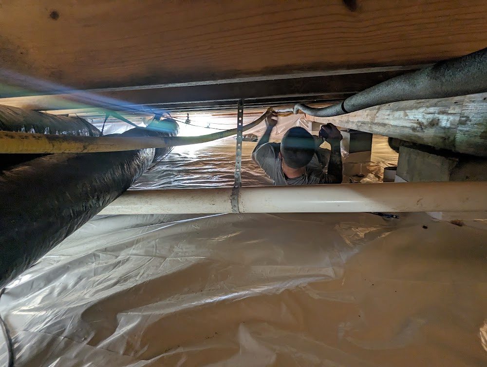 Low view along lined crawl space toward worker and equipment