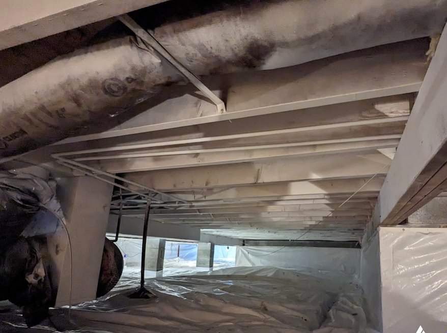 Joists and pipes above a white crawl space liner