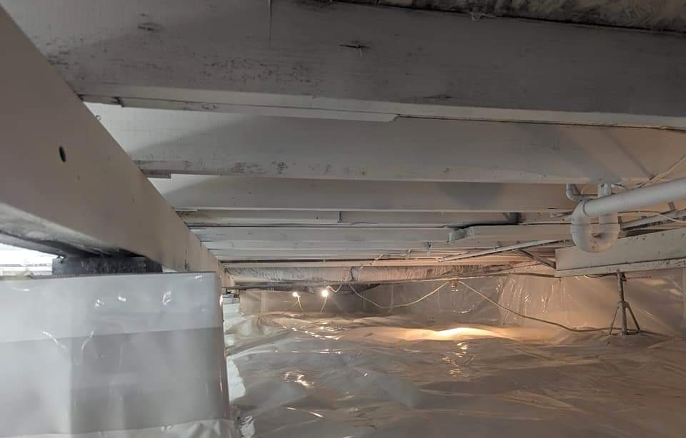 Wide white-lined crawl space beneath joists and pipes