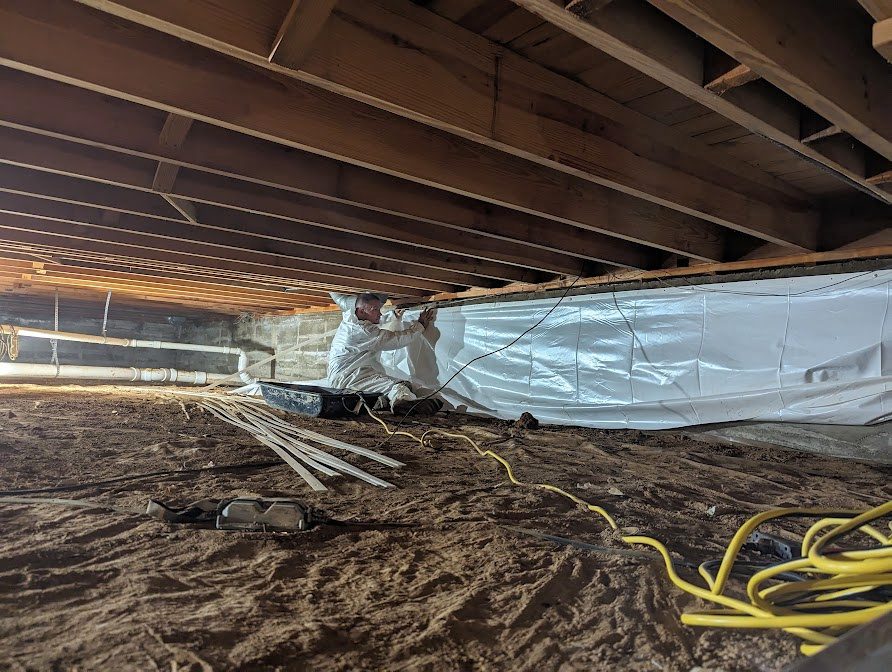 Watertight worker installing perimeter liner above bare crawl space soil