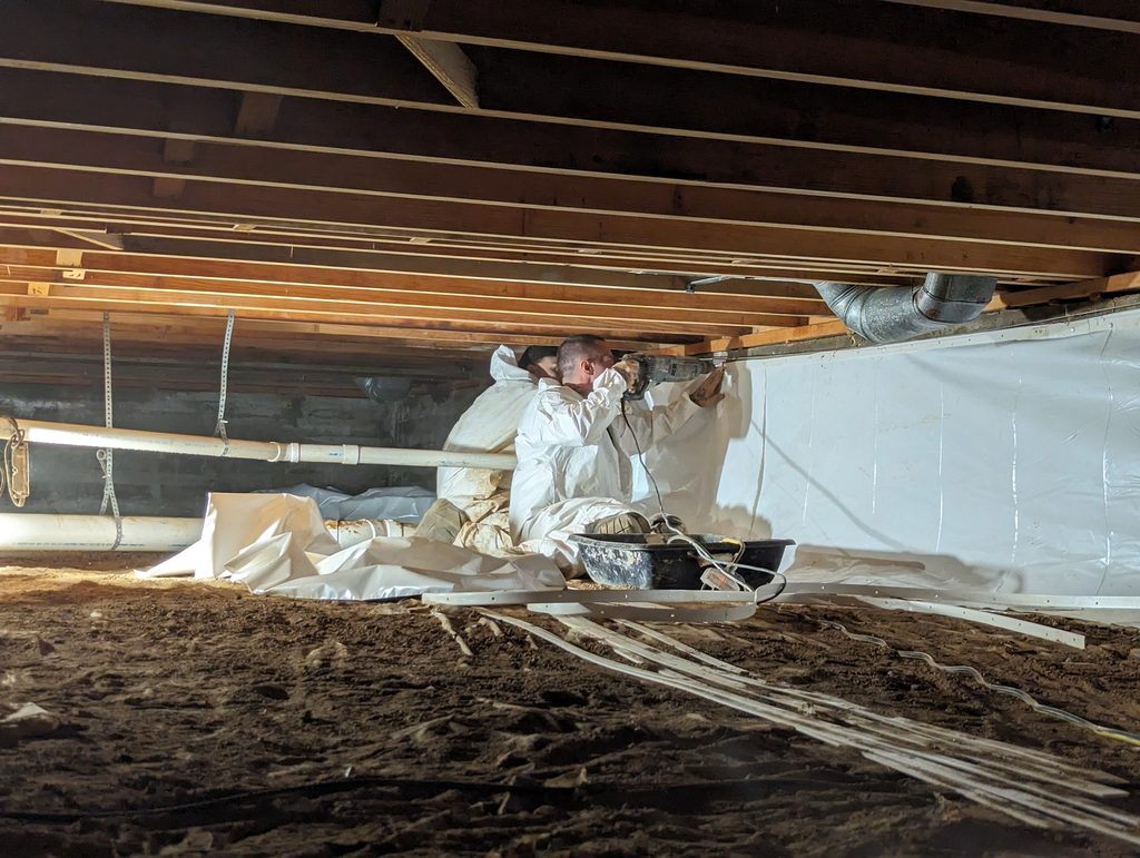 Two Watertight crew members fastening white liner along a crawl space wall