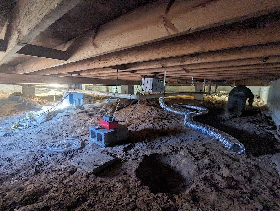 Worker near exposed crawl space trench and drainage pipe