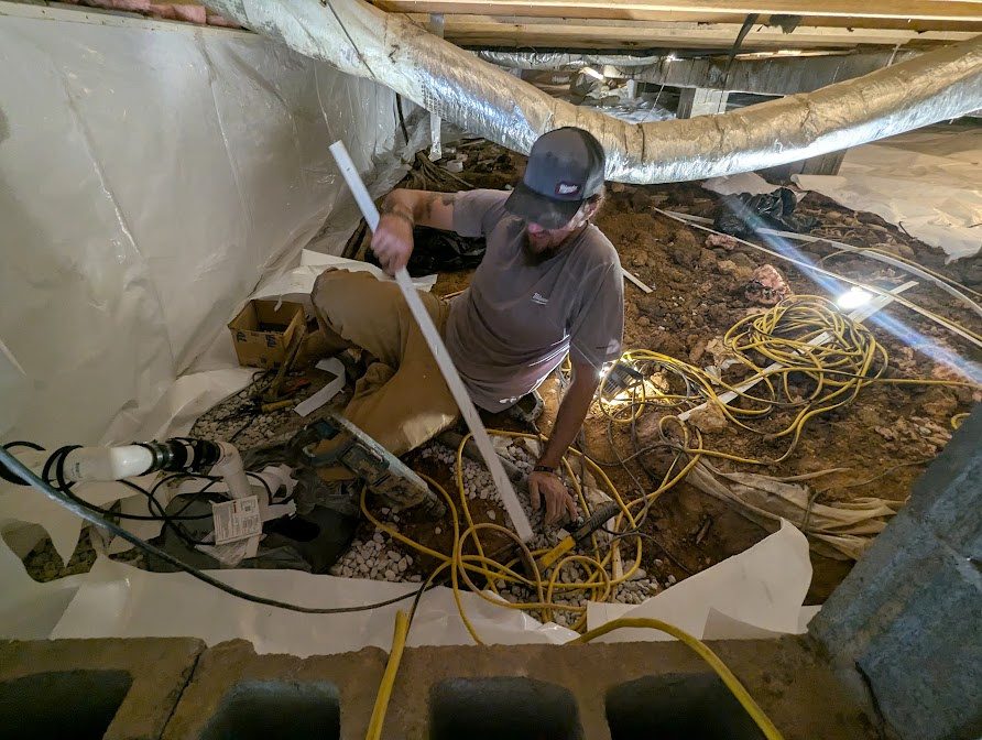 Worker standing at open crawl space excavation with equipment