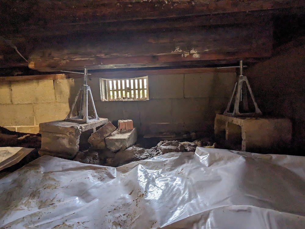 Crawl space with dark joists, temporary supports and liner