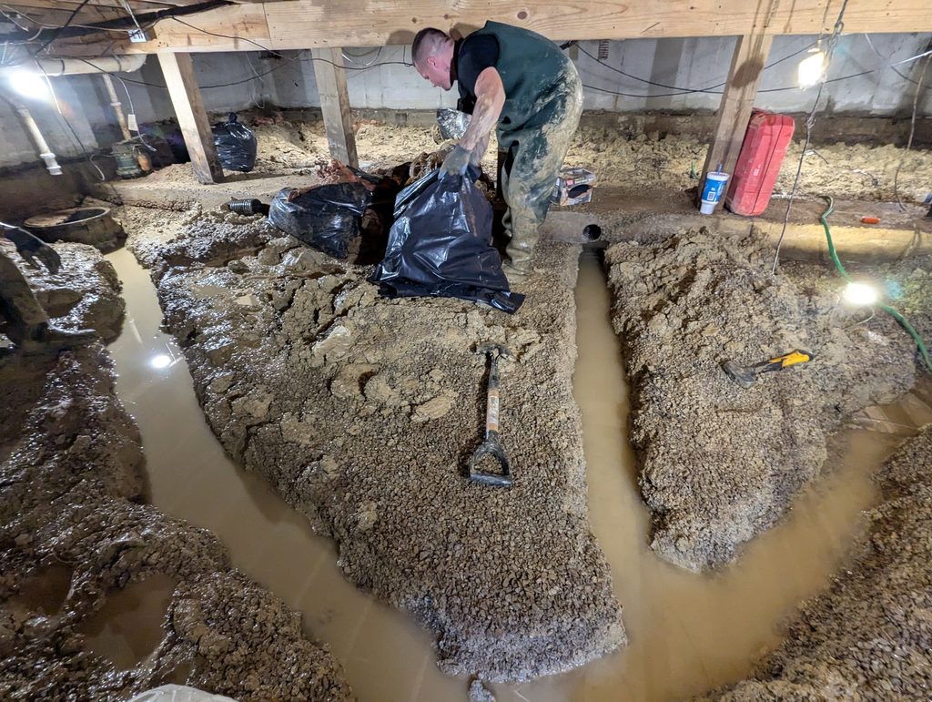 Worker removing material beside water-filled crawl space trenches