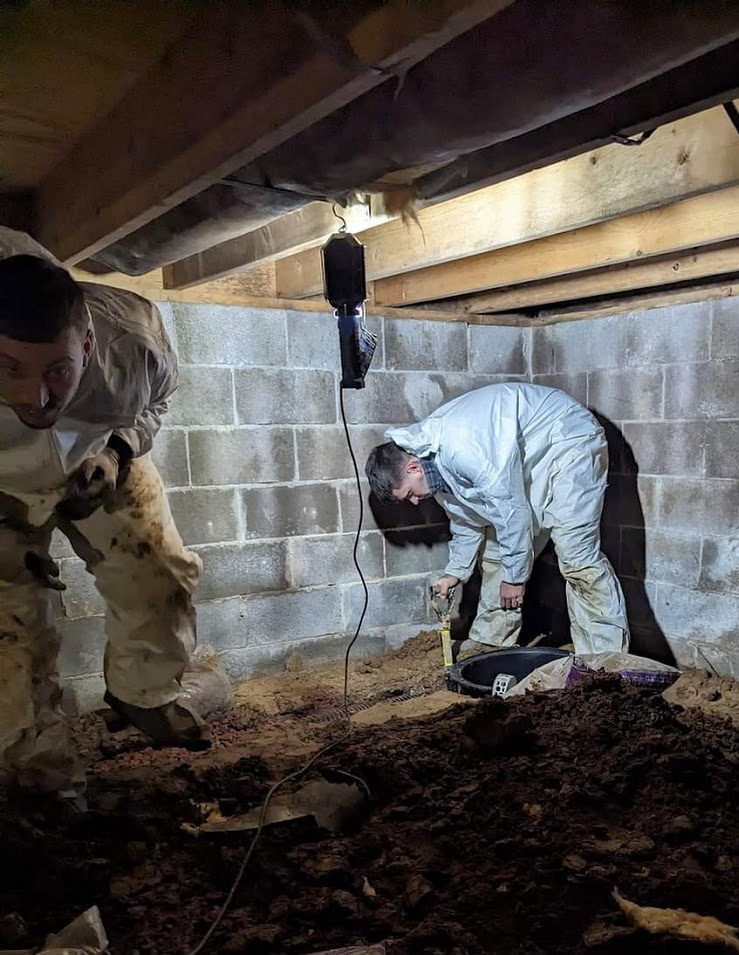 Coveralled worker digging in crawl space corner