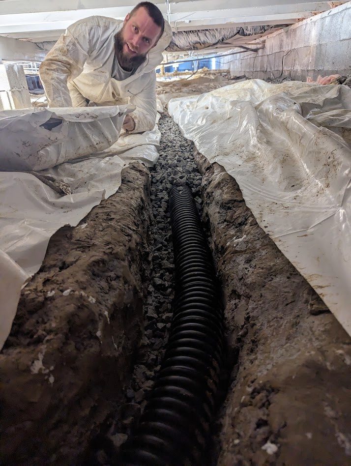 Watertight worker behind an open trench containing black drainage pipe