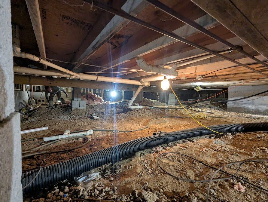 Wide crawl space with black drainage pipe on exposed soil