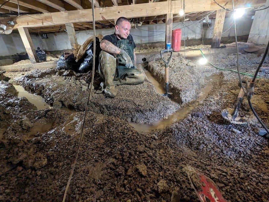 Worker beside water-filled crawl space trenches