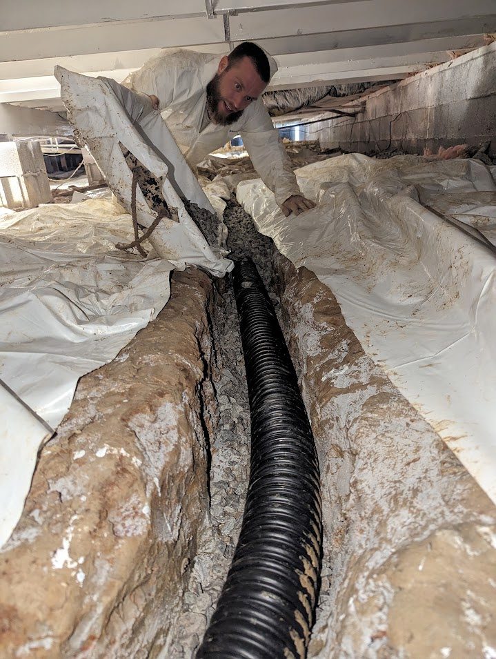 Worker beside corrugated pipe in crawl space trench