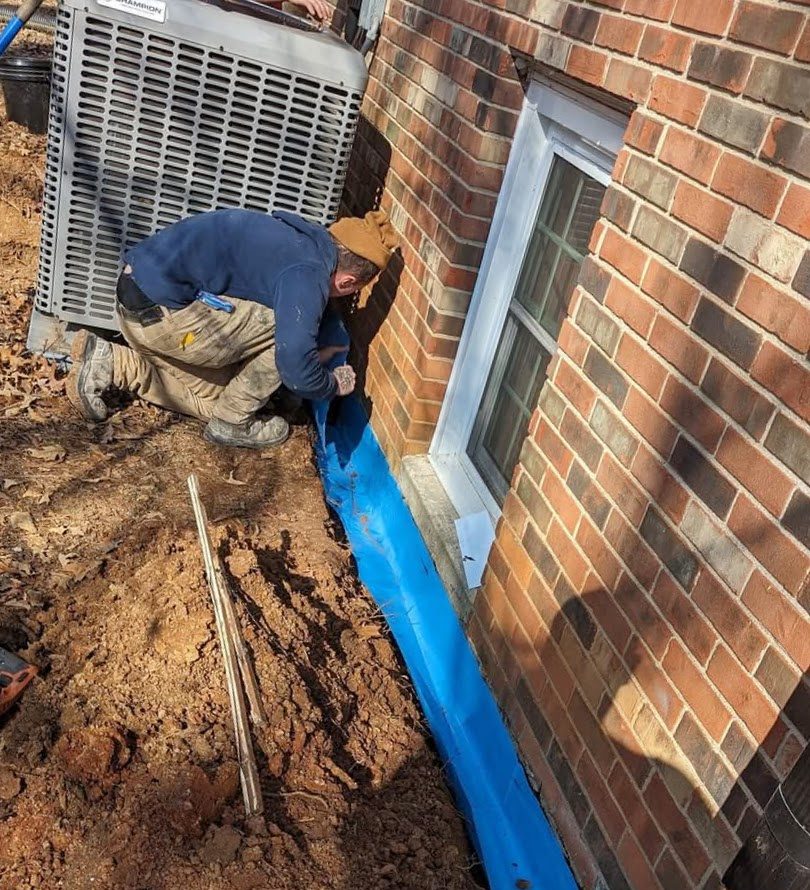 Worker applying blue material along brick foundation