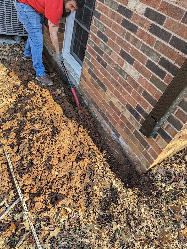 An excavation beside a basement window in a brick wall