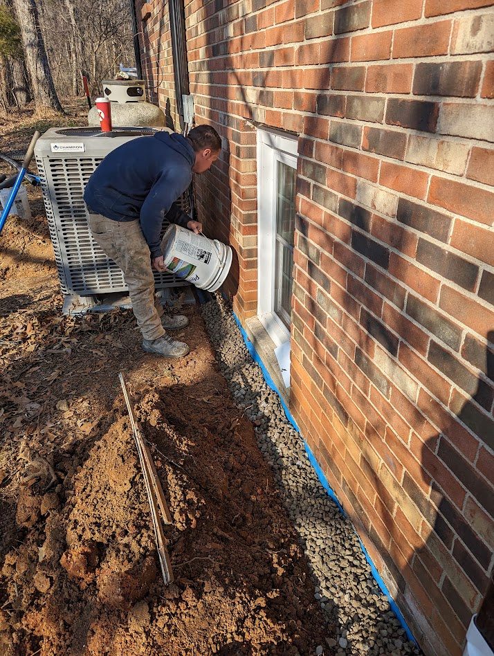A worker pouring from a bucket into a trench along a brick wall