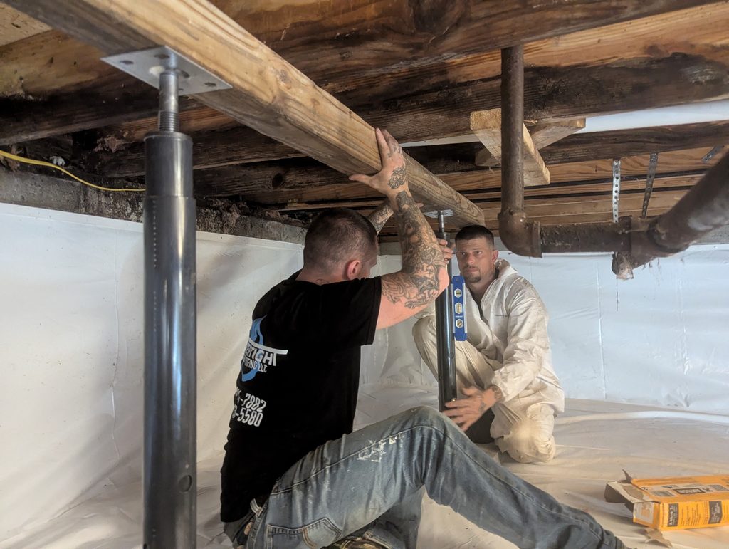 Two workers setting a steel support post under a timber beam