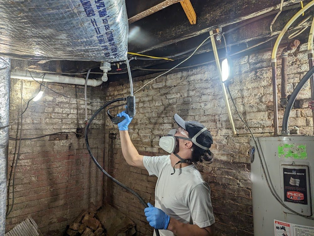 Worker wearing respirator treating basement ceiling