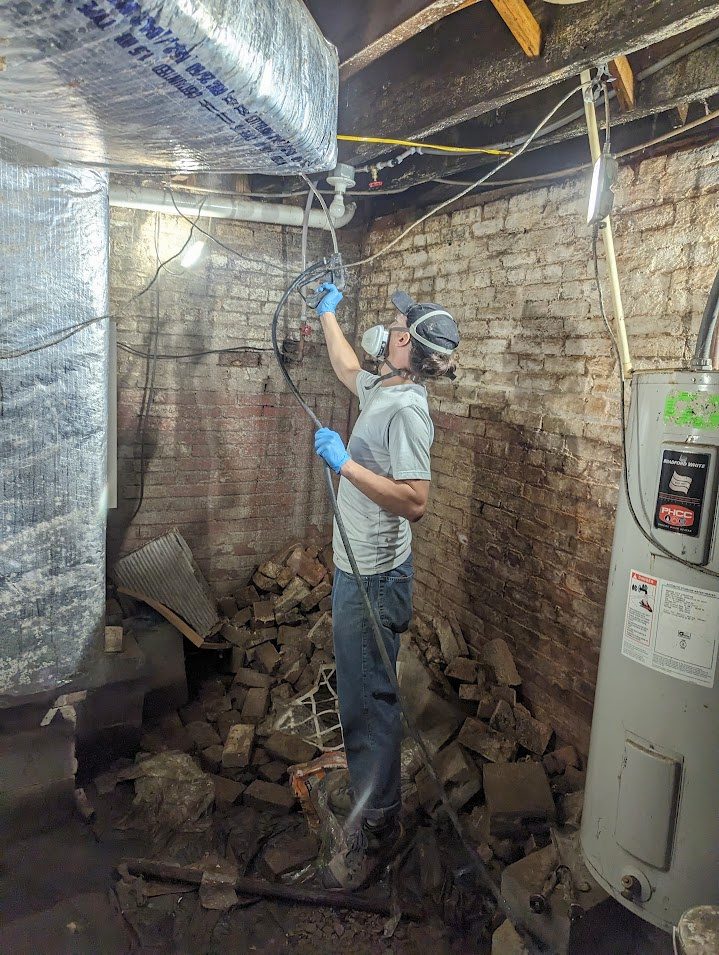 A worker in a respirator spraying the framing in a brick basement