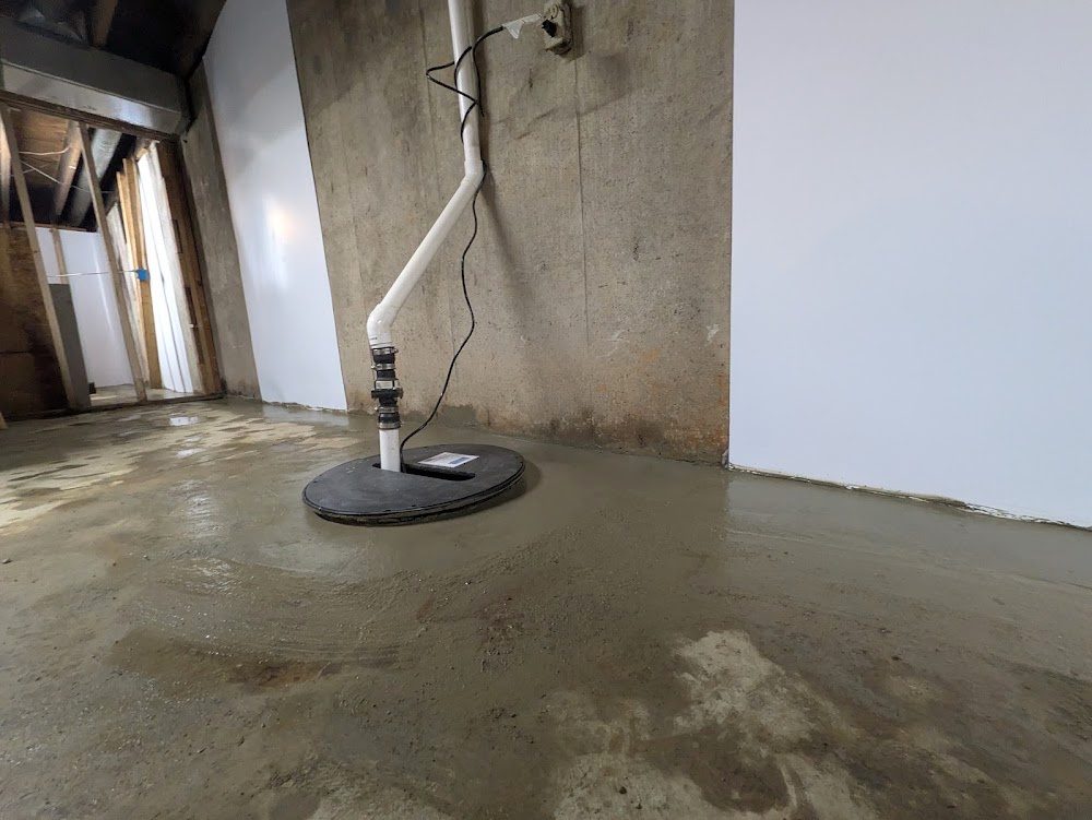 Sealed sump lid and discharge pipe beside a white-lined basement wall